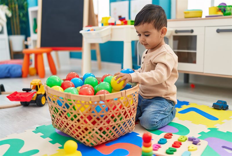 A Playgroup child sorting coloured balls into a basket on the play mat